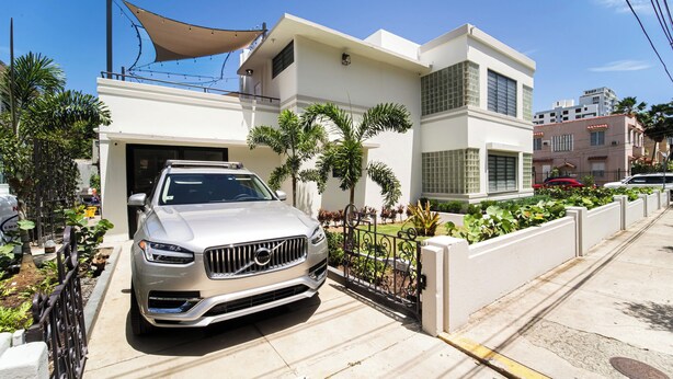 A modern two-story house with a driveway, parked cars, and a garden with palm trees. - Stunning Villa - 1 Block from the Beach (San Juan)