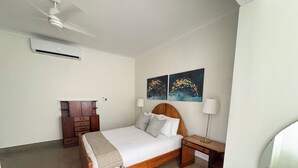 A bedroom with a wooden bed, a nightstand, a lamp, a dresser, and two wall-mounted paintings. - Stunning Villa - 1 Block from the Beach (San Juan)