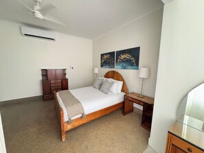 Ein Schlafzimmer mit einem hölzernen Bett, einem Nachttisch, einer Lampe, einer Kommode und zwei an der Wand hängenden Bildern.
