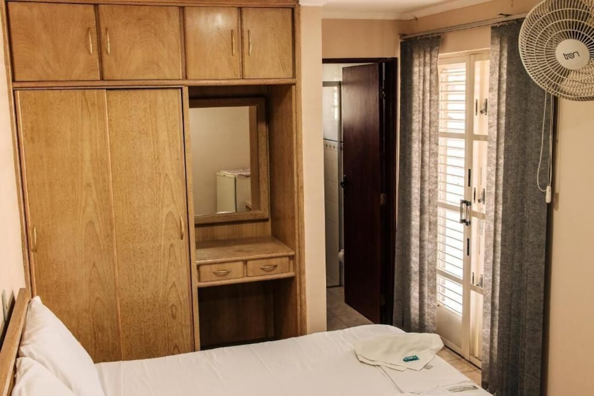 A bedroom with a wooden wardrobe, a bed with white bedding, and a fan.