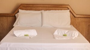 A bed with a wooden headboard, two pillows, and two folded towels on a white bedspread.