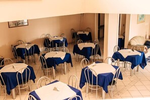 A dining area with multiple tables and chairs, arranged in a spacious room with a tiled floor. - Niv s Hotel (Monte Siao)