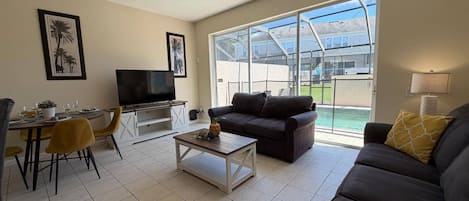 Un salon comprenant un téléviseur, un canapé, une table basse et un coin repas avec des chaises et une table.