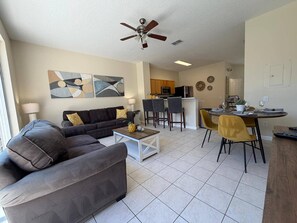 A living room with a sofa, coffee table, and a dining area with chairs and a table. - Wp2355 - 3BR Townhome Resort Access Near Parks (Kissimmee)