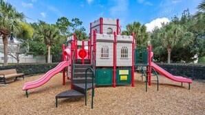 A playground with slides and climbing structures, surrounded by trees and a bench. - Wh2596 - 6BR House at Windsor Hills Resort (Kissimmee)