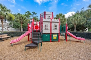 Ein Spielplatz mit Rutschen und Klettergerüsten, umgeben von Bäumen und einer Bank.