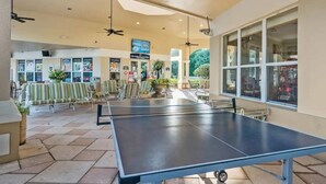 A spacious indoor area with ping pong tables, seating, and a view of the outside through large windows. - Wh2596 - 6BR House at Windsor Hills Resort (Kissimmee)