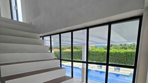 Una escalera lleva a un balcón con vista a una piscina y follaje.