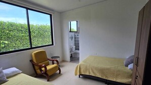 Habitación con dos camas, una silla, un armario, un ventilador de techo y una ventana con vistas a la vegetación.