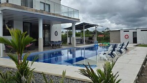 Un edificio moderno con piscina, mobiliario exterior y un patio cubierto.