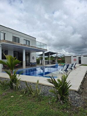 A modern building with a swimming pool, outdoor seating, and a covered patio area.