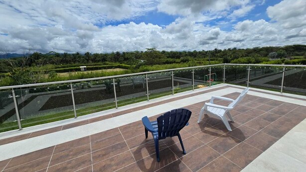 Una terraza con vistas a un jardín, barandilla de cristal y dos sillas.