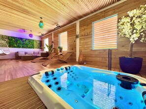 Een kamer met een houten plafond, een jacuzzi, een bank en een muur met een groene plant.
