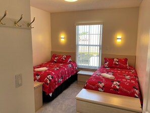 Une chambre avec deux lits, chacun recouvert d’une couette aux motifs de Mickey Mouse, une fenêtre avec des barreaux et des lampes fixées au mur.