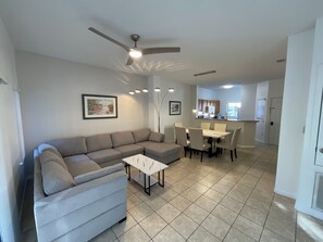 A living room with a sectional sofa, a coffee table, and a dining area with a table and chairs. - Stunning 3 Beds Newly Townhouse (Kissimmee)