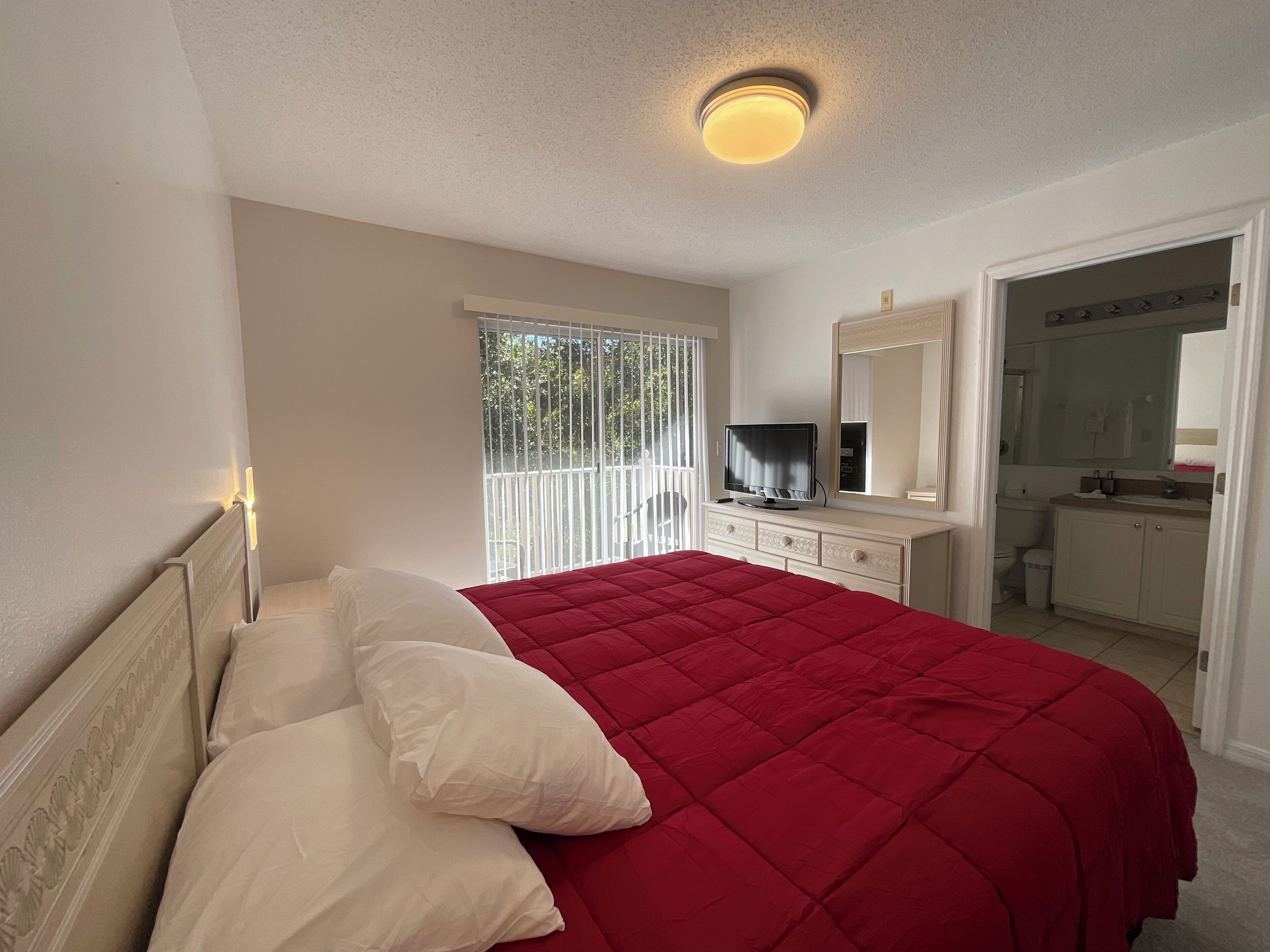 Ein Schlafzimmer mit einem Bett, einem Fernseher, einem Spiegel und einem durch eine offene Tür einsehbaren Badezimmer.