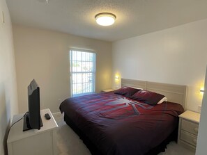 A hotel room with a bed, bedside table, and a television on a stand. - Stunning 3 Beds Newly Townhouse (Kissimmee)