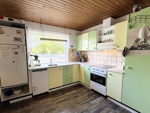 A kitchen with wooden ceiling, green cabinets, a white refrigerator, and a window with a view of greenery.