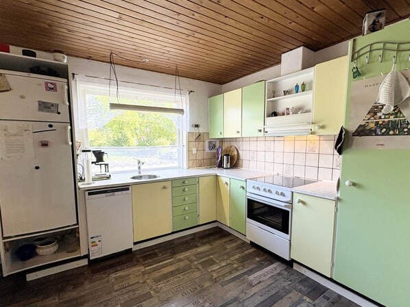 Cocina con techo de madera, armarios verdes, un refrigerador blanco y una ventana con vista a follaje.