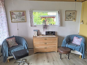A cozy room with two blue armchairs, a wooden dresser, and a window with a view of greenery. - 6 Person Holiday Home in Nykobing M (Nykobing Mors)