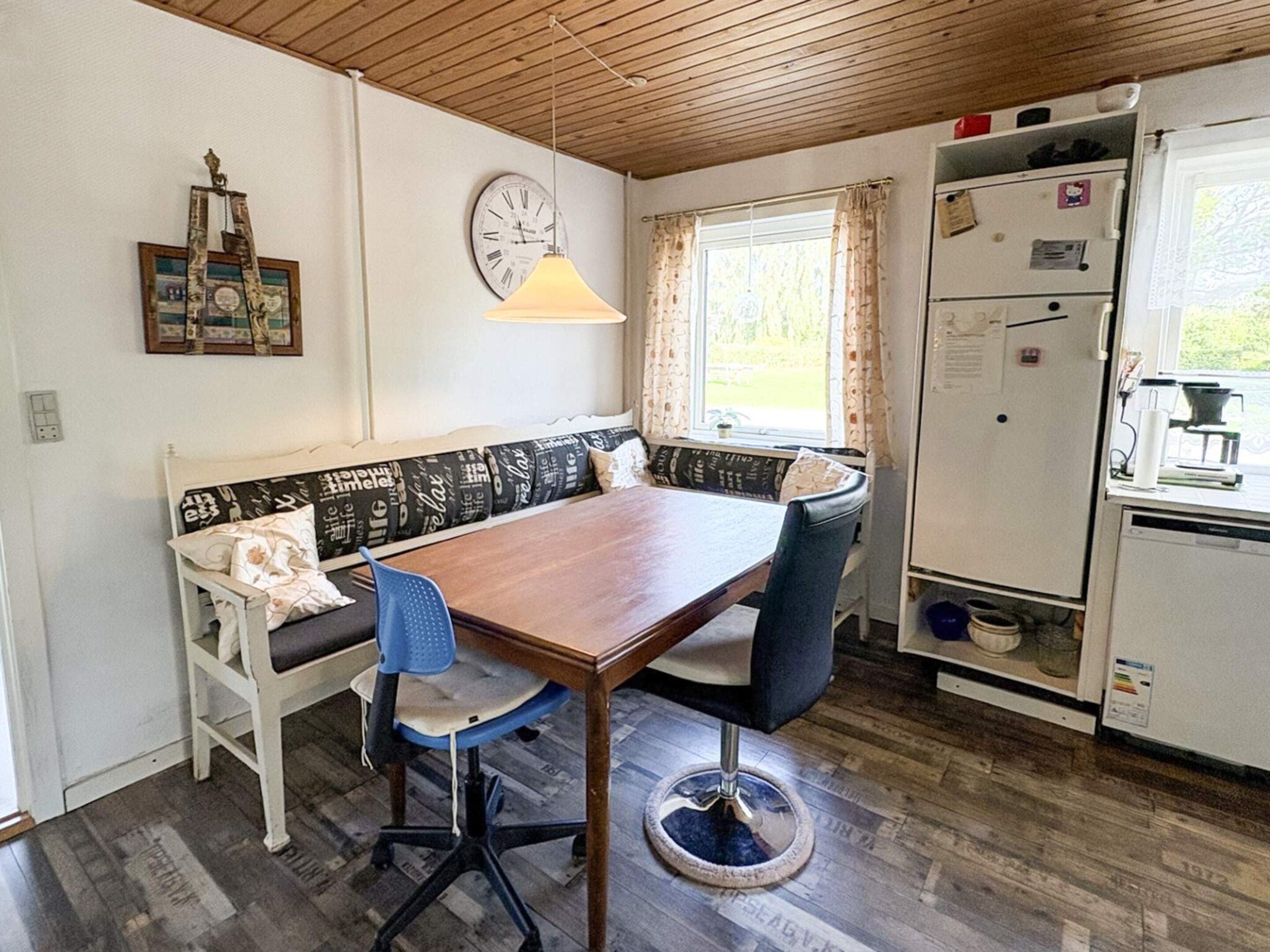 A compact kitchen with a wooden table, a bench, and a refrigerator.