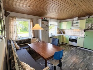 Une cuisine chaleureuse avec un plafond en bois, une table à manger avec une chaise bleue et une fenêtre avec des rideaux.