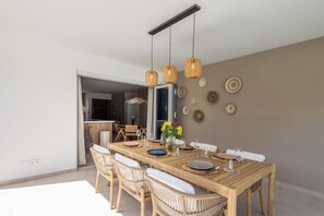 A dining area with a wooden table, wicker chairs, and a modern pendant light fixture. - Prime Location: New Home in Jan Thiel with Private Pool (Willemstad)