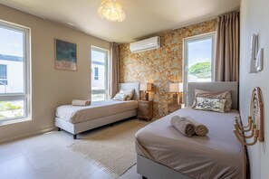 A bedroom with two beds, a large window, an air conditioning unit, and a patterned wall. - Prime Location: New Home in Jan Thiel with Private Pool (Willemstad)