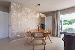 A dining area with a round wooden table, four chairs, a hanging light fixture, and a patterned wallpaper. - Prime Location: New Home in Jan Thiel with Private Pool (Willemstad)