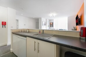 A modern kitchen with a double sink, white cabinets, and a red kettle on the counter. - Modern 5 Bed Flat in Thornaby Road For Big Groups (Stockton-on-Tees)