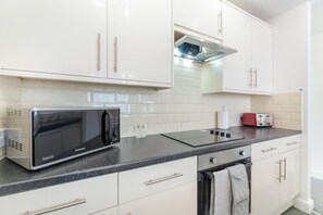 Eine moderne Küche mit weißen Schränken, einer schwarzen Mikrowelle, einem Toaster und einem Edelstahlbackofen.