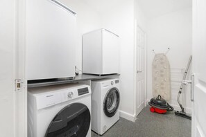 A laundry area with a washing machine, dryer, and ironing board. - Modern 5 Bed Flat in Thornaby Road For Big Groups (Stockton-on-Tees)
