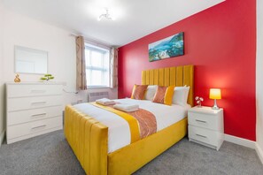 Ein Hotelzimmer mit einem Bett, einem Nachttisch, einer Kommode, einem Fenster mit Vorhängen und einem Gemälde an der Wand.