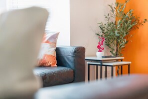 A living room with a leather sofa, a small side table, and a potted plant. - Modern 5 Bed Flat in Thornaby Road For Big Groups (Stockton-on-Tees)