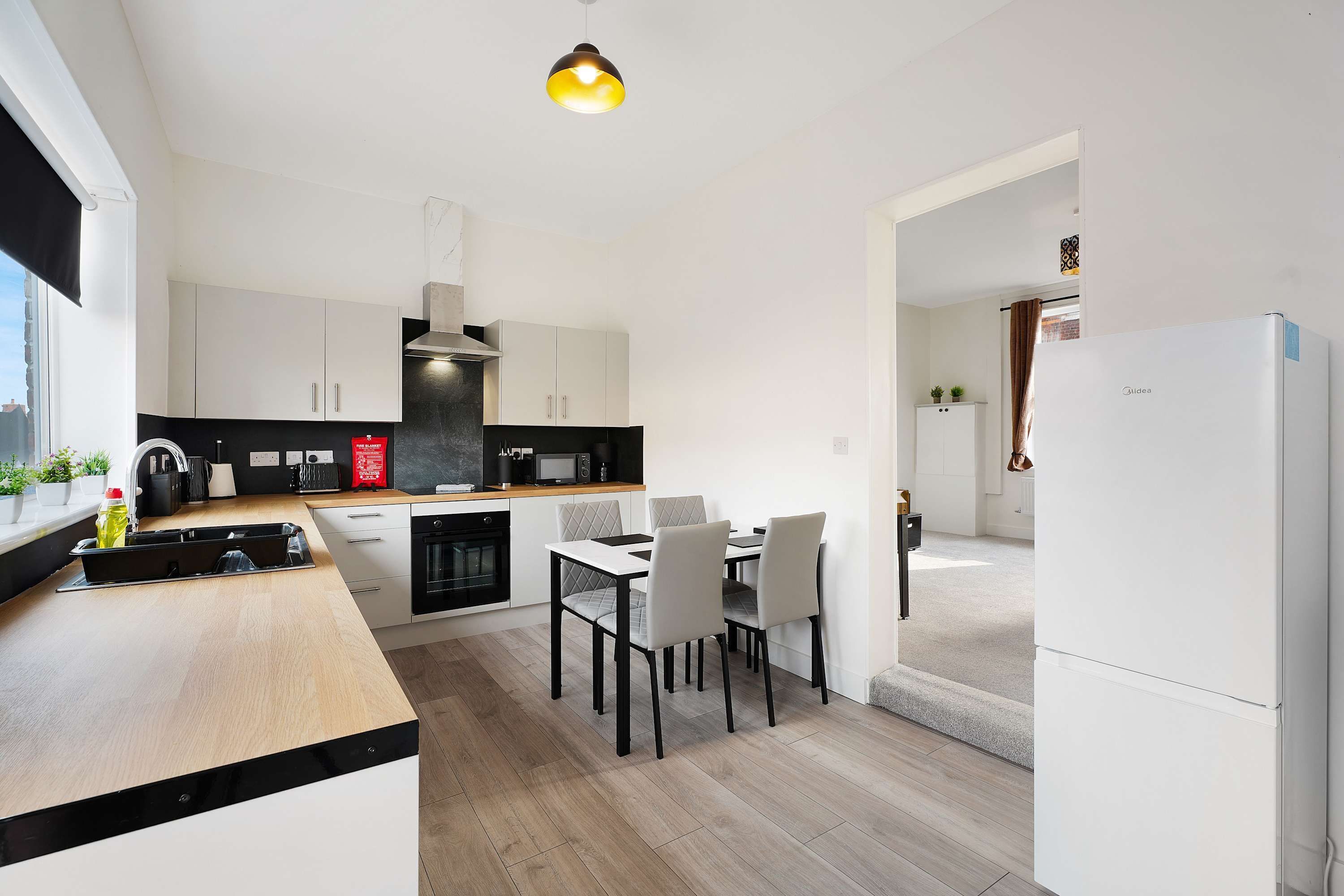 Une cuisine moderne avec des meubles blancs, un plan de travail noir et un coin repas comprenant une table et des chaises.