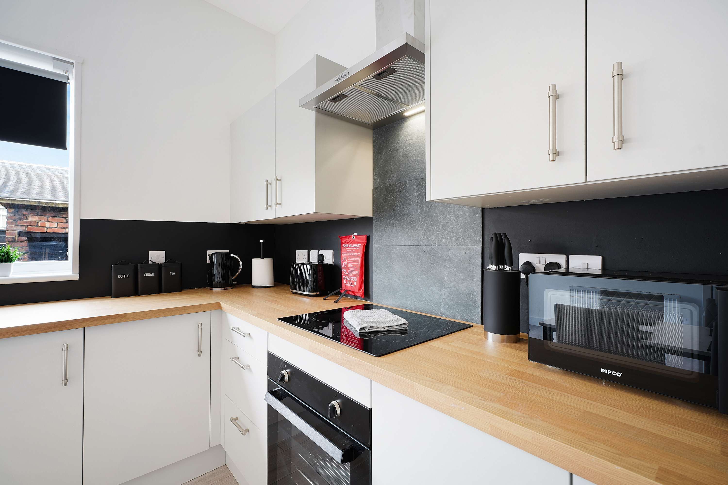 A modern kitchen with white cabinets, a black countertop, a built-in oven, and a window with a view of a brick building.