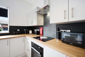 Une cuisine moderne avec des meubles blancs, un plan de travail noir, un four encastré et une fenêtre donnant sur un immeuble en briques.