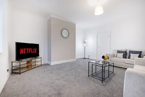 Un salon équipé d’un téléviseur à écran plat, d’une table basse, d’un canapé et d’un lampadaire.