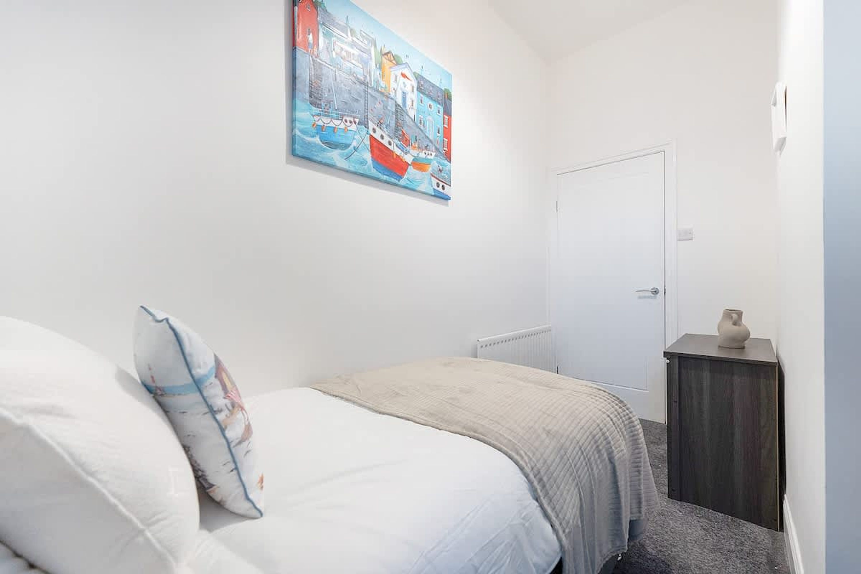 A bedroom with a bed, a nightstand, a door, and a painting on the wall.