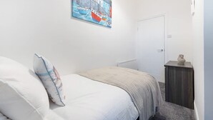 A bedroom with a bed, a nightstand, a door, and a painting on the wall. - Newly Refurbished Near the Coast Sleeps 5 (Newbiggin-by-the-Sea)