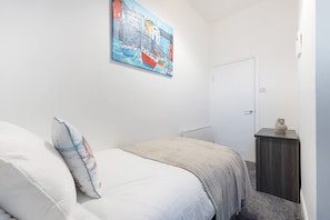 Ein Schlafzimmer mit Bett, Nachttisch, Tür und einem Bild an der Wand.