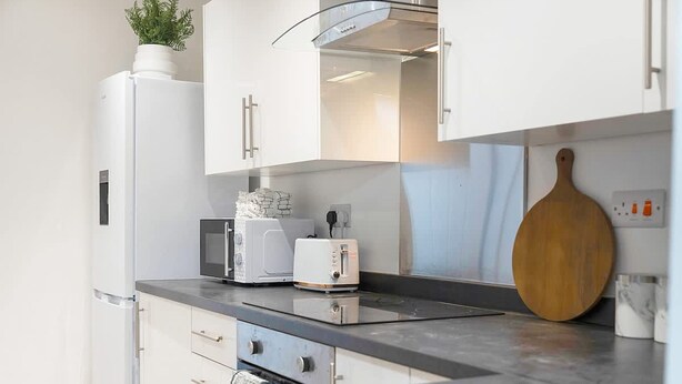 A modern kitchen with white cabinets, a built-in oven, a toaster, and a wooden cutting board. - Newly Refurbished Near the Coast Sleeps 5 (Newbiggin-by-the-Sea)