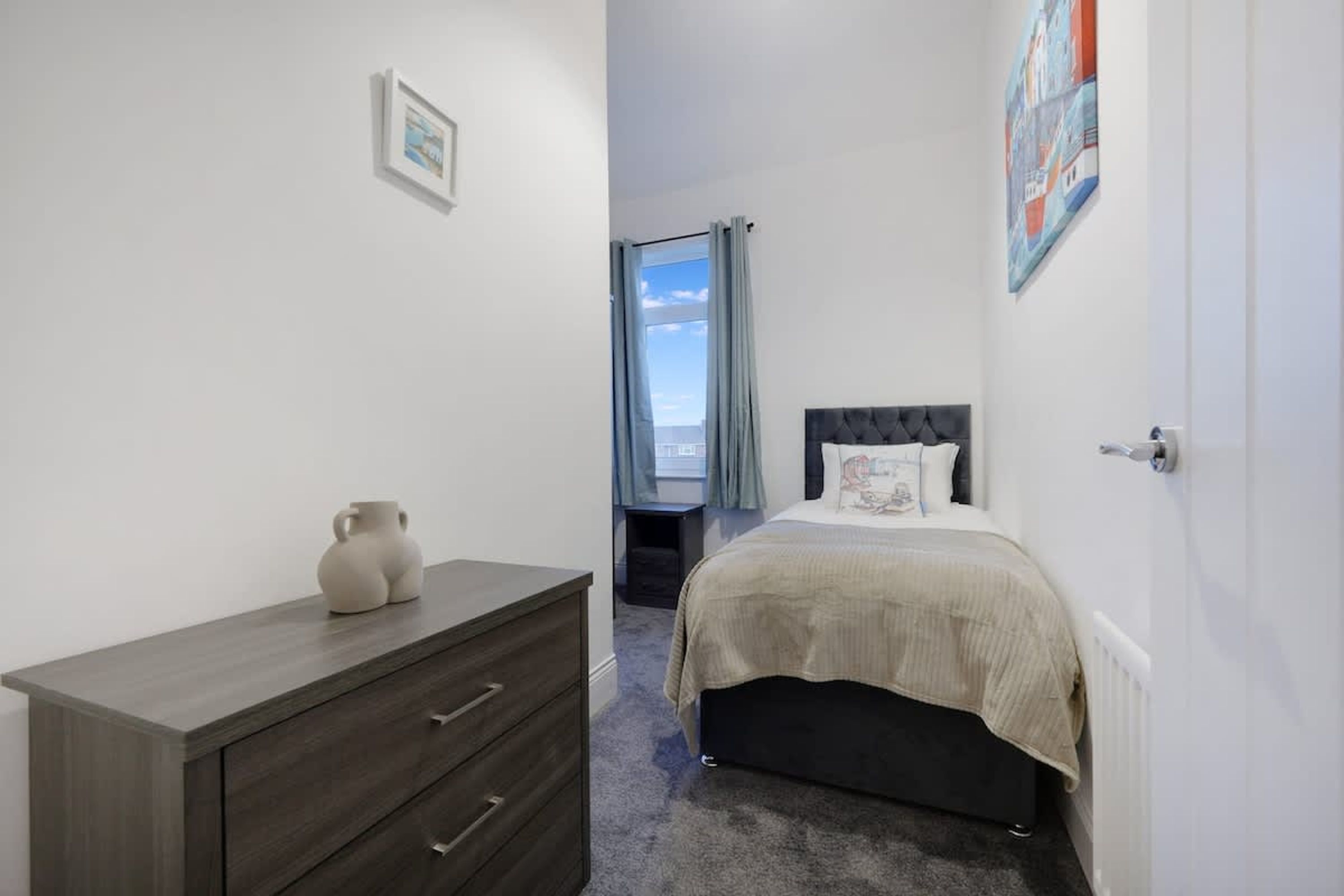 Une chambre à coucher avec un lit, une commode, une fenêtre avec des rideaux et une vue sur le ciel.
