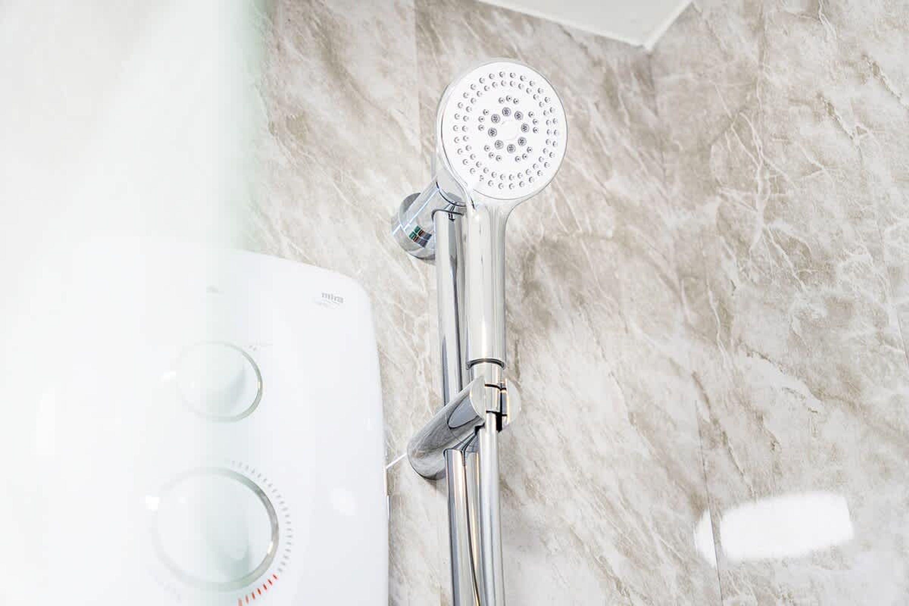 A shower with a handheld showerhead and a control panel with two knobs.