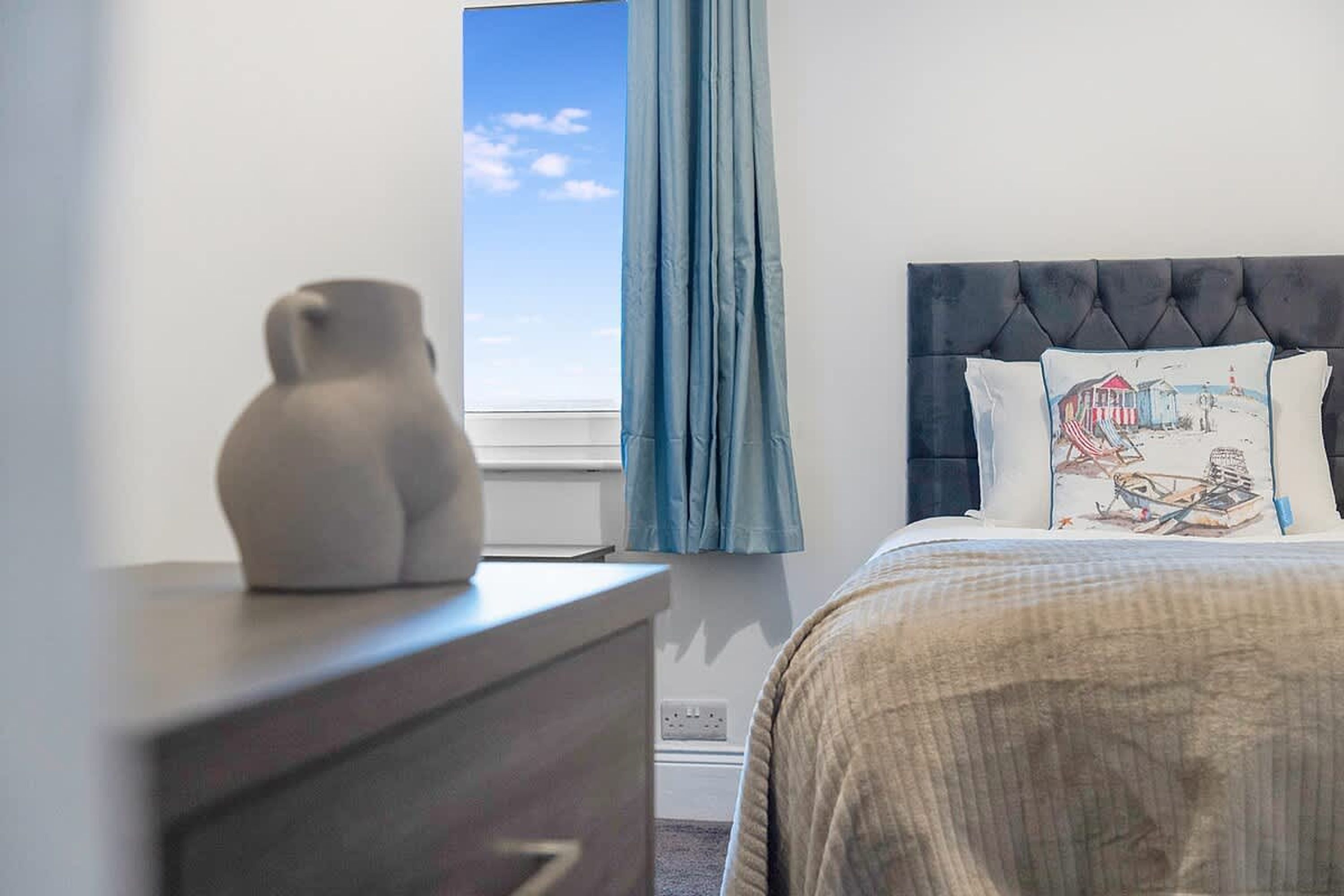 Een slaapkamer met een bed, een dressoir, een raam met gordijnen en uitzicht op de lucht.