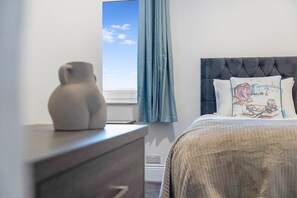 Ein Schlafzimmer mit einem Bett, einem Schminktisch, einem Fenster mit Vorhängen und Blick zum Himmel.