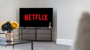 A living room with a television displaying 'NETFLIX' on the screen, a coffee table with a vase of flowers, and a carpeted floor. - Newly Refurbished Near the Coast Sleeps 5 (Newbiggin-by-the-Sea)