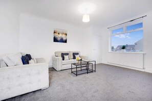 Ein modernes Wohnzimmer mit einem weißen Sofa, einem kleineren Sofa, einem Couchtisch und einem großen Fenster.