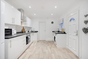 Une cuisine moderne avec des meubles blancs, un four à micro-ondes, un four traditionnel et un lave-linge.