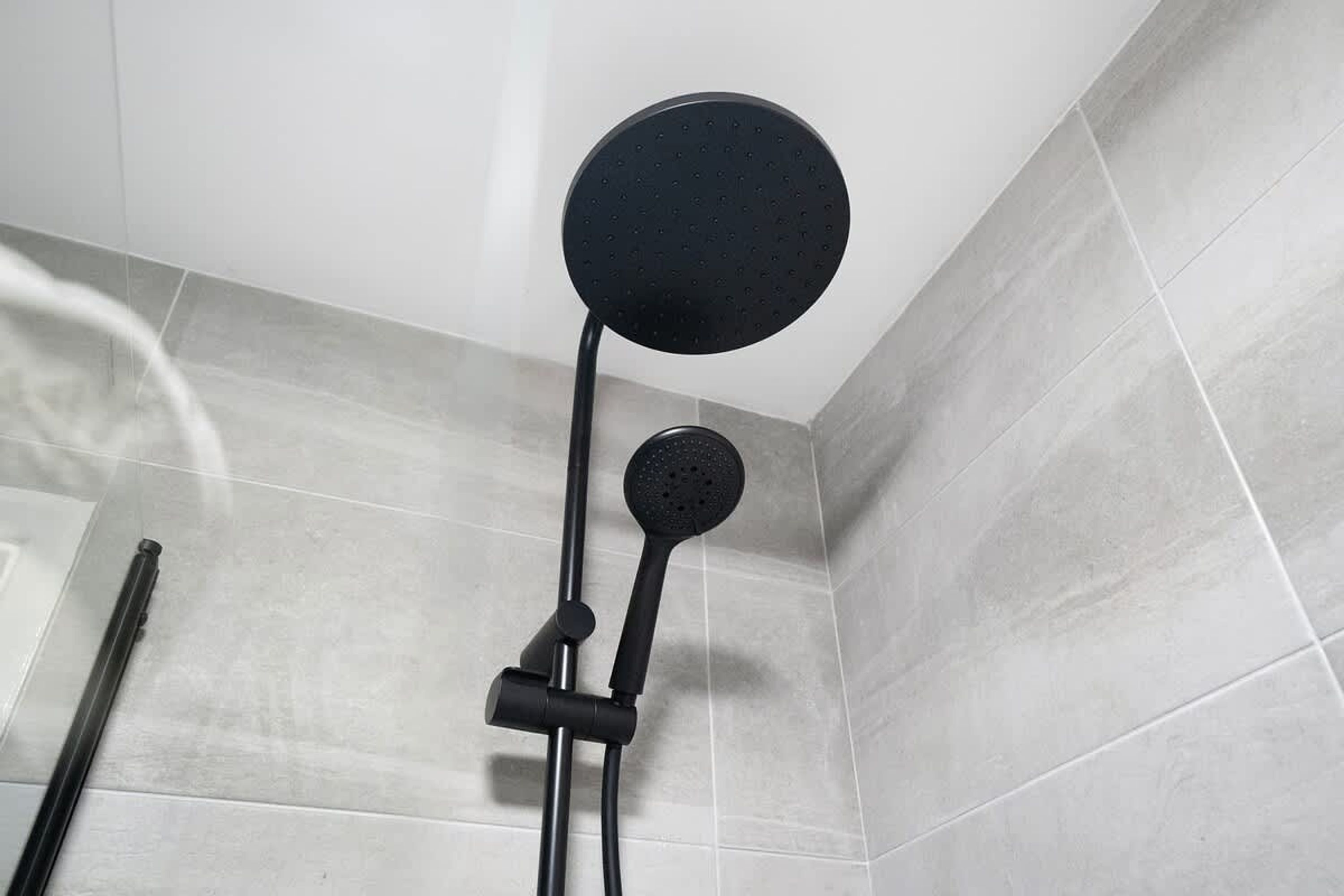 A shower with a roundhead showerhead mounted on a wall, a handheld showerhead attached to a flexible hose, and a vertical bar for support.